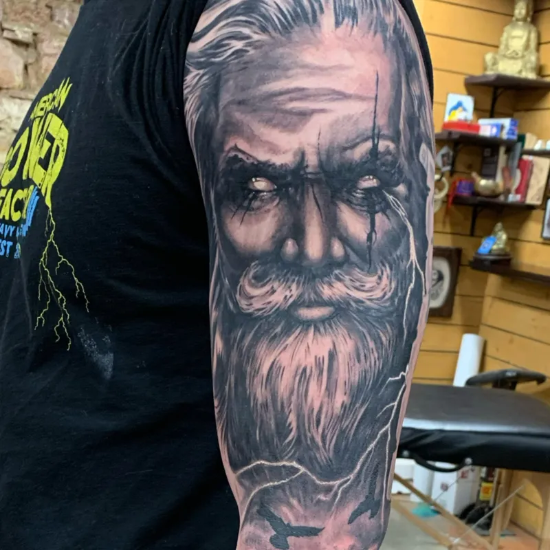 Black and gray portrait tattoo of a bearded old man with lightning and ravens down the arm