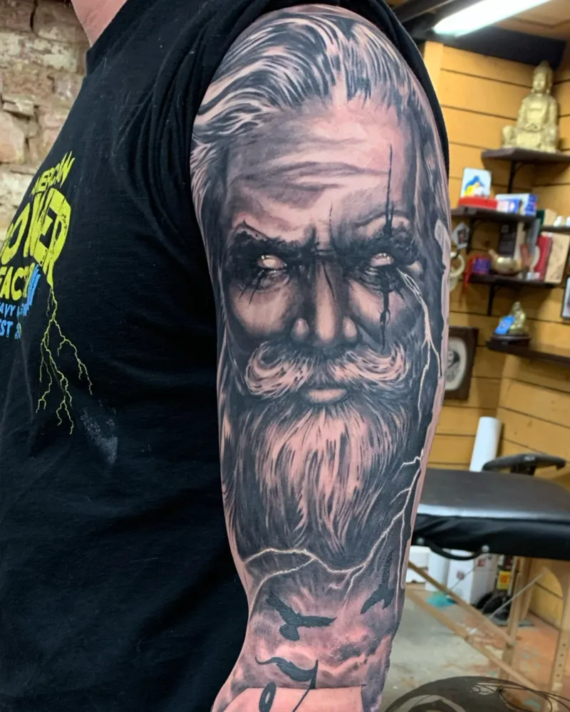 Black and gray portrait tattoo of a bearded old man with lightning and ravens down the arm