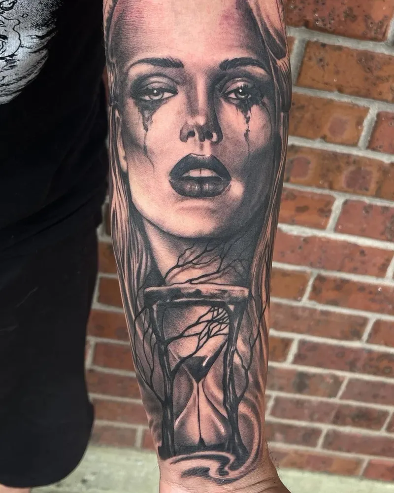 Black and gray surrealism tattoo blending a woman's crying face into an hourglass with bare branches