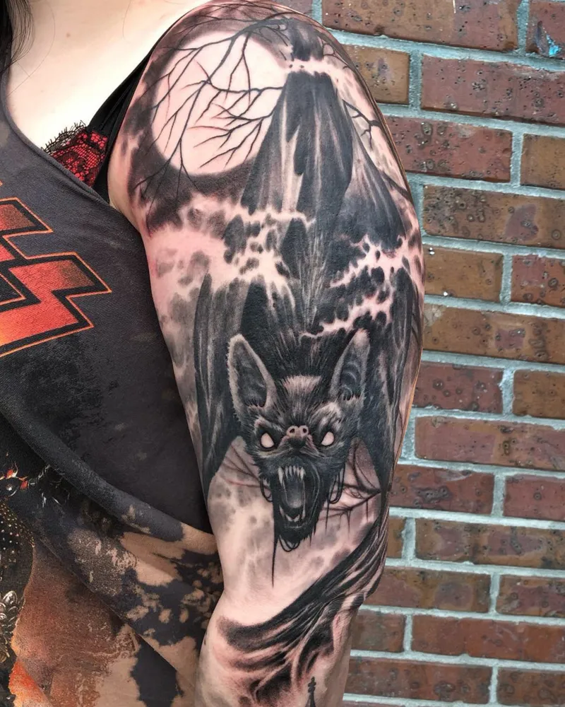 Black and gray tattoo of a bat in flight beneath a full moon and bare branches