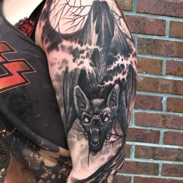 Black and gray tattoo of a bat in flight beneath a full moon and bare branches