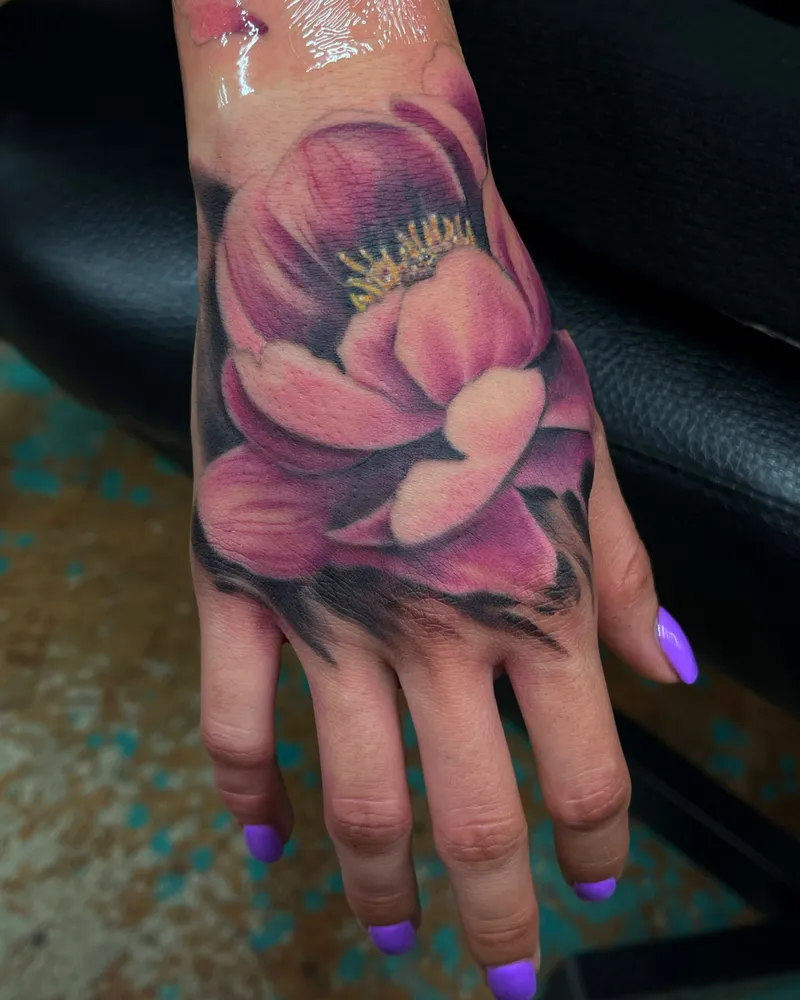 Fresh color tattoo of a large pink and purple lotus flower covering the back of the hand