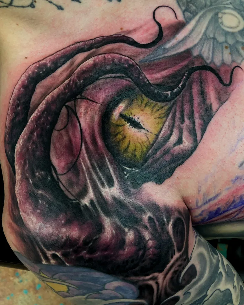 Bioorganic color tattoo of a yellow reptilian eye peering out from torn, fleshy pink and purple skin on the chest