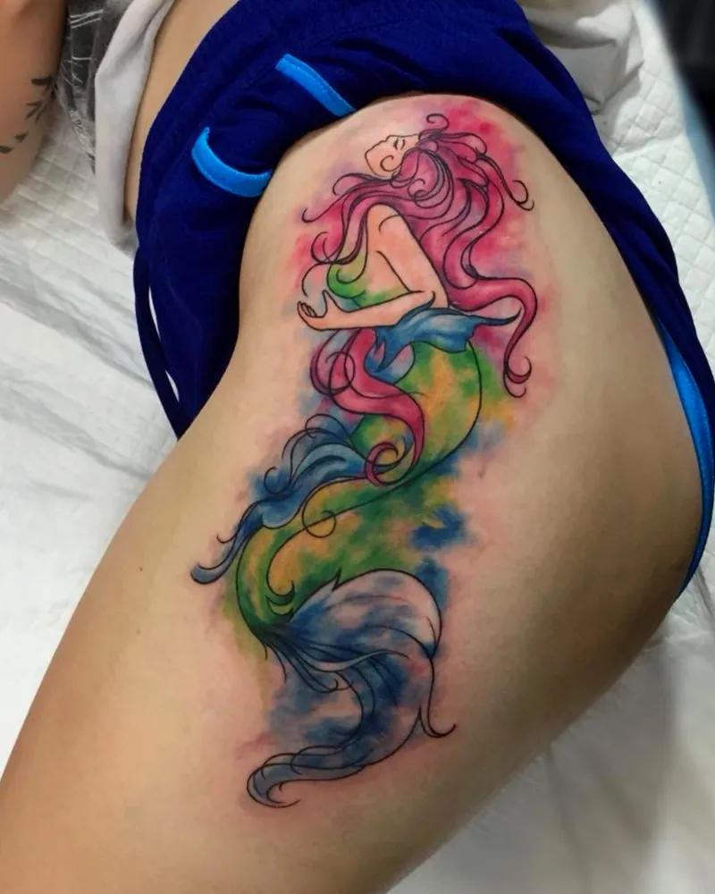 Watercolor-style mermaid tattoo on the hip with flowing pink hair and a blue, green, and yellow tail