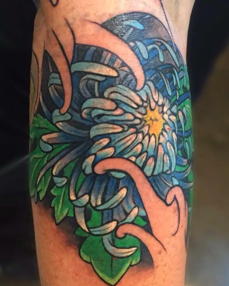 Color Japanese chrysanthemum tattoo on the leg with blue and white petals, a yellow center, and green leaves