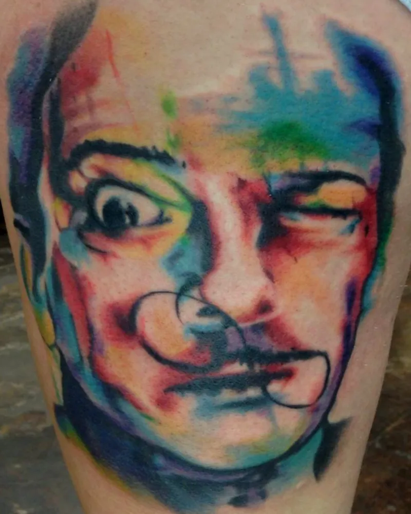 Watercolor-style abstract portrait tattoo with splattered color and loose linework across the face