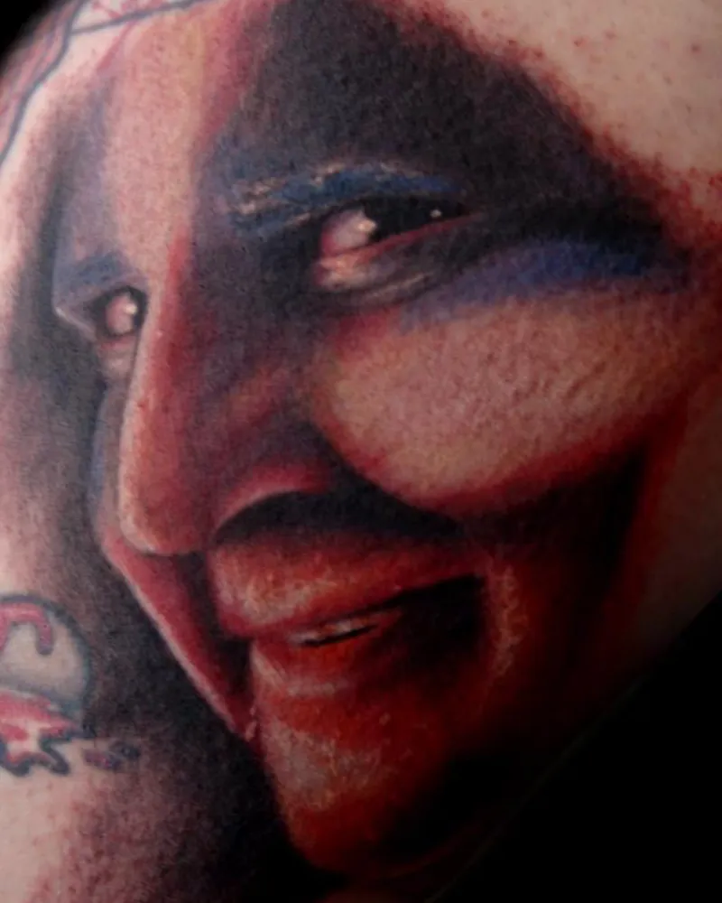 Close-up detail of a color tattoo of a screaming demon face with fangs and blood-streaked skin