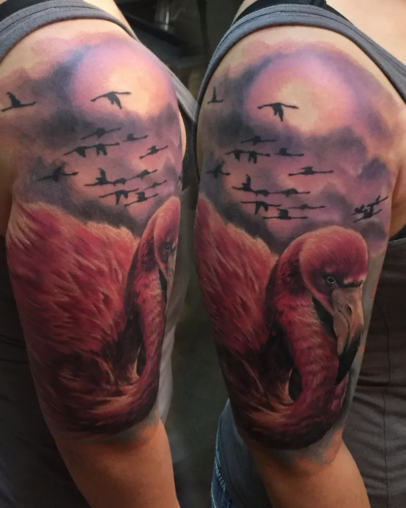 Color flamingo tattoo with a sunset sky and flock of birds in flight, shown on both arms