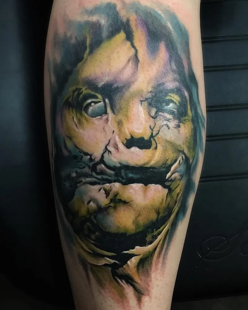 Color surrealist portrait tattoo with a torn, molten face rendered in teal, yellow, and purple watercolor tones