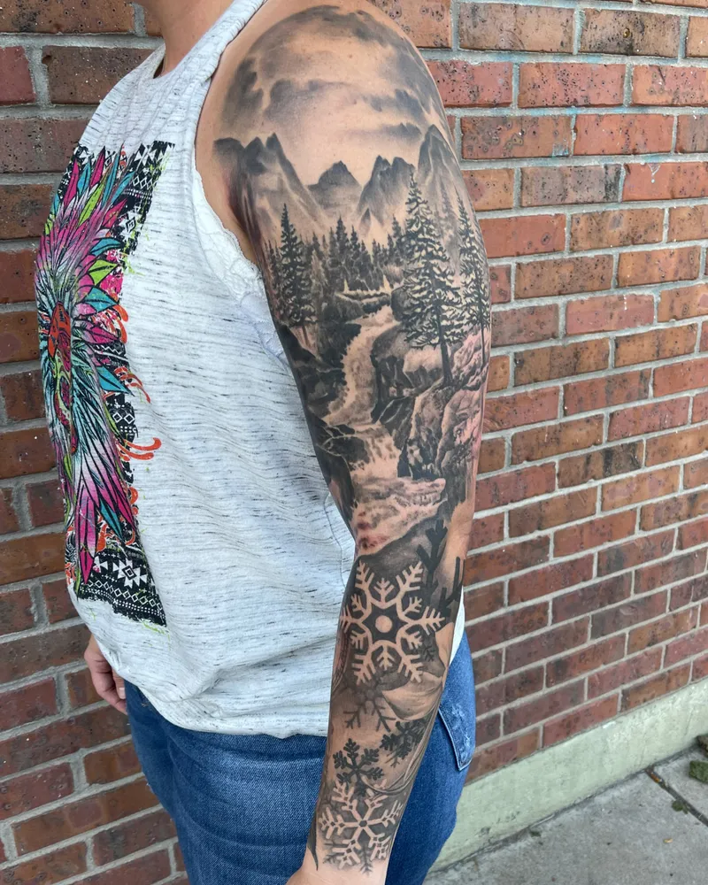 Full sleeve with misty mountains, a pine forest stream, and snowflakes down the forearm, viewed from the front