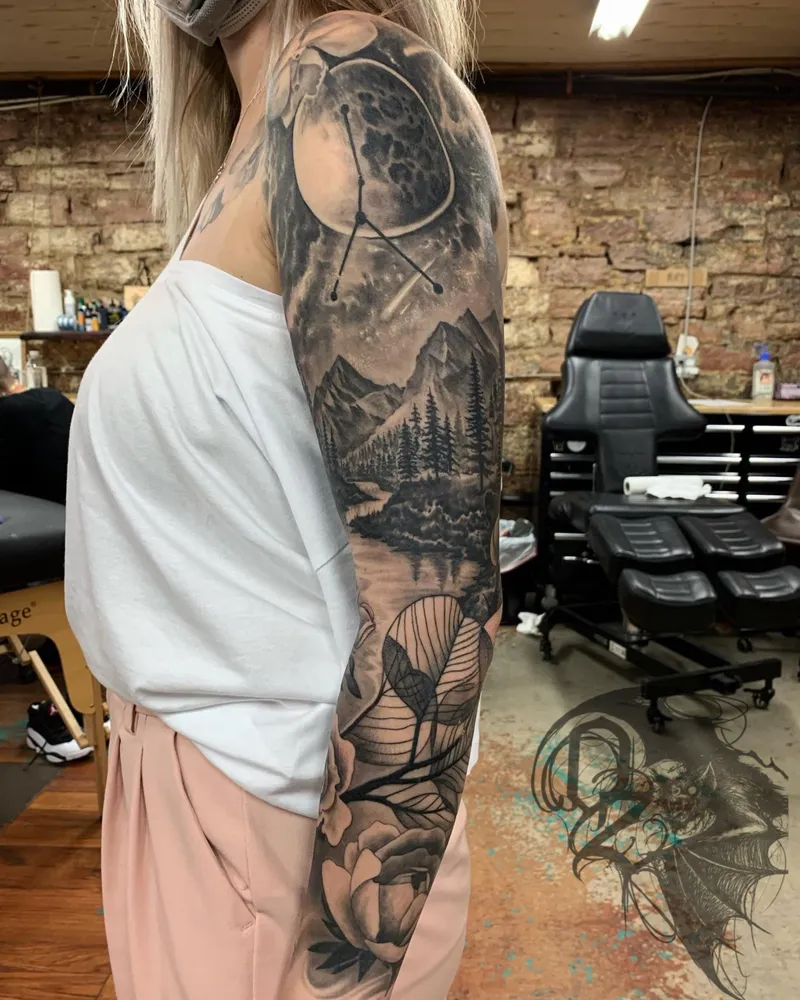 Full sleeve with a moon and constellation over a mountain lake, flowing into linework leaves and peonies on the forearm
