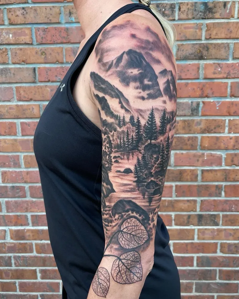 Half sleeve mountain landscape with a rushing river and pine trees, ending in aspen leaves on the forearm