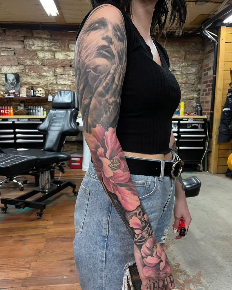 Full sleeve pairing a black and gray veiled face with pink peonies and a skull down the forearm