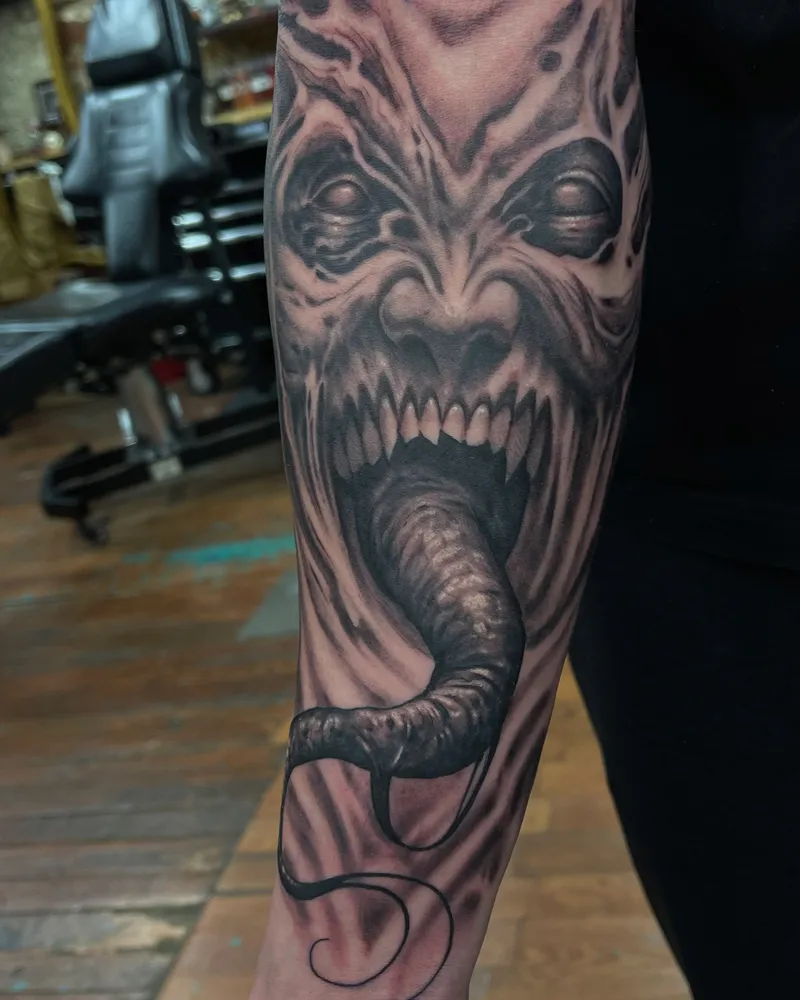 Freehand demon face tattoo on the forearm with a long tongue curling downward