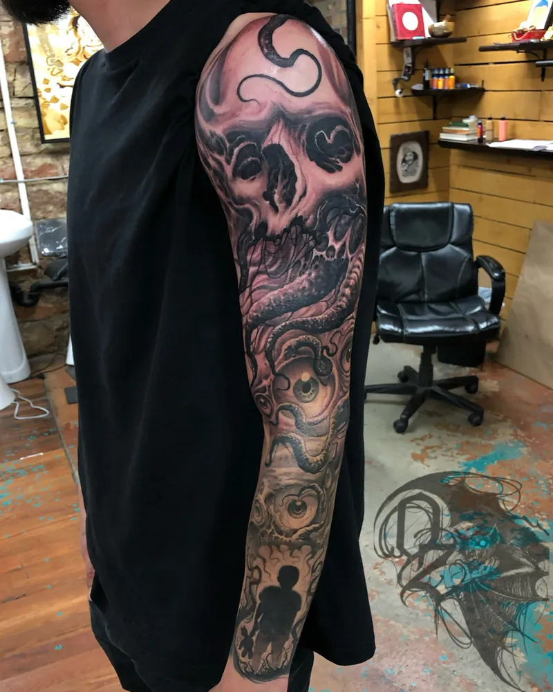 Freehand tattoo of a skull and coiled serpent flowing into a large eye on the upper arm