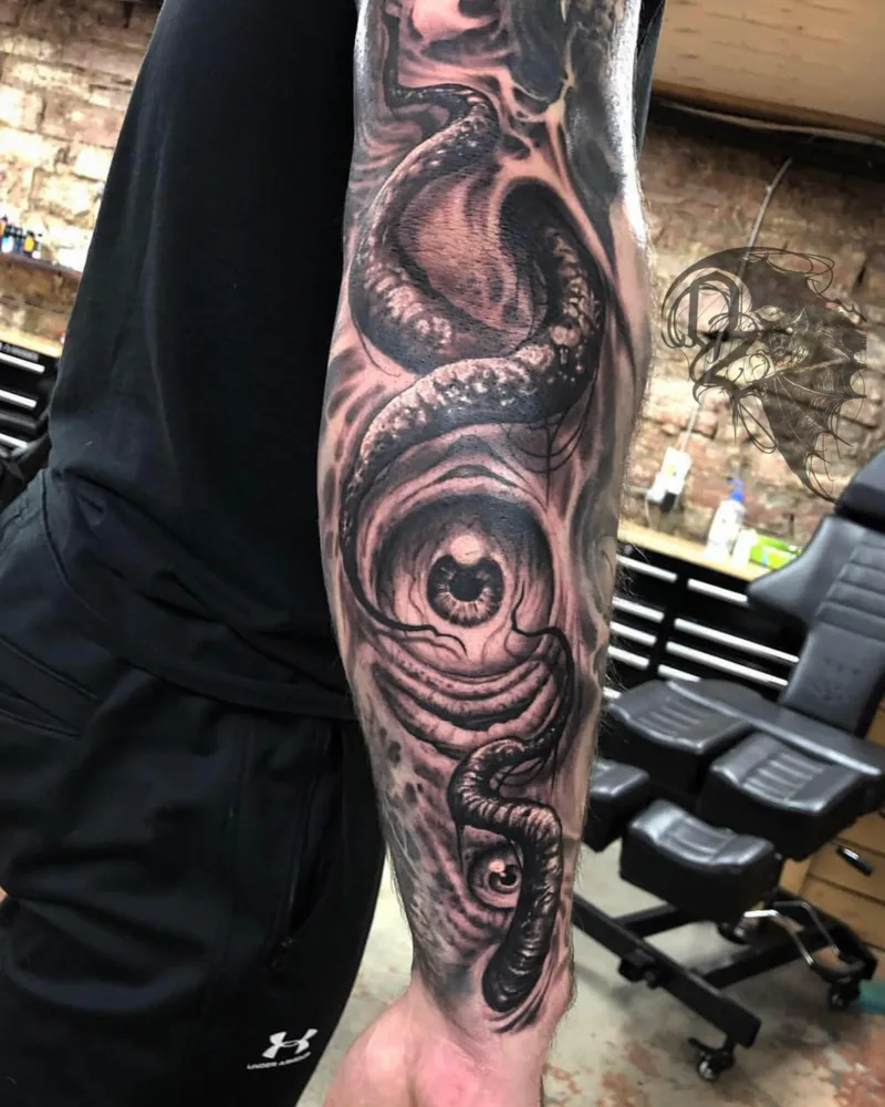 Close-up of a bioorganic freehand tattoo with a coiled serpent and eye on the forearm
